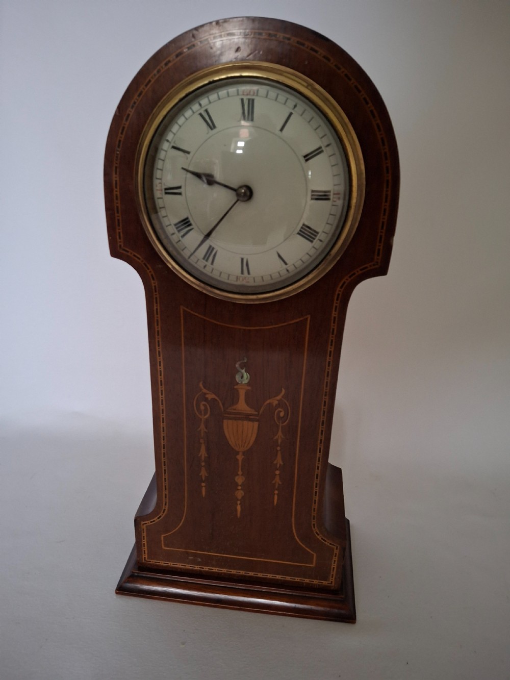 An Art Nouveau mahogany mantel clock featuring a balloon-shaped case with inlaid urn marquetry, boxwood stringing, a circular white dial with Roman numerals, and a brass bezel. View VII