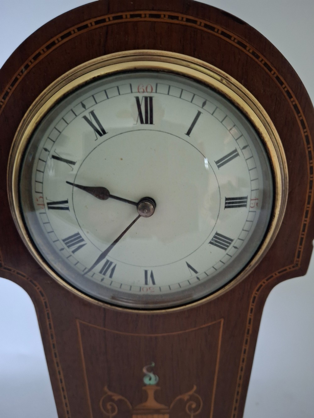 An Art Nouveau mahogany mantel clock featuring a balloon-shaped case with inlaid urn marquetry, boxwood stringing, a circular white dial with Roman numerals, and a brass bezel. View VIII