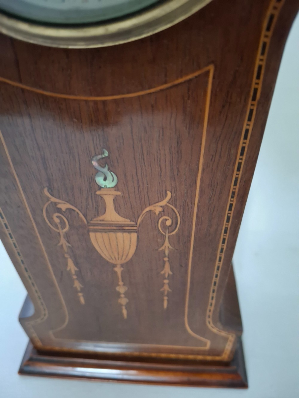 An Art Nouveau mahogany mantel clock featuring a balloon-shaped case with inlaid urn marquetry, boxwood stringing, a circular white dial with Roman numerals, and a brass bezel. View IX