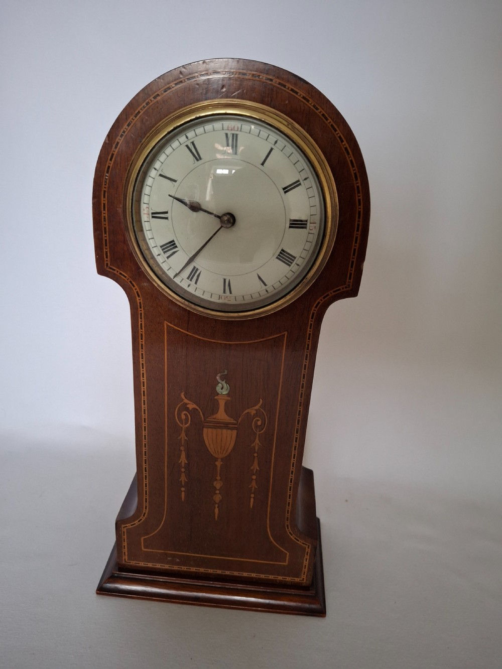 An Art Nouveau mahogany mantel clock featuring a balloon-shaped case with inlaid urn marquetry, boxwood stringing, a circular white dial with Roman numerals, and a brass bezel. View XI