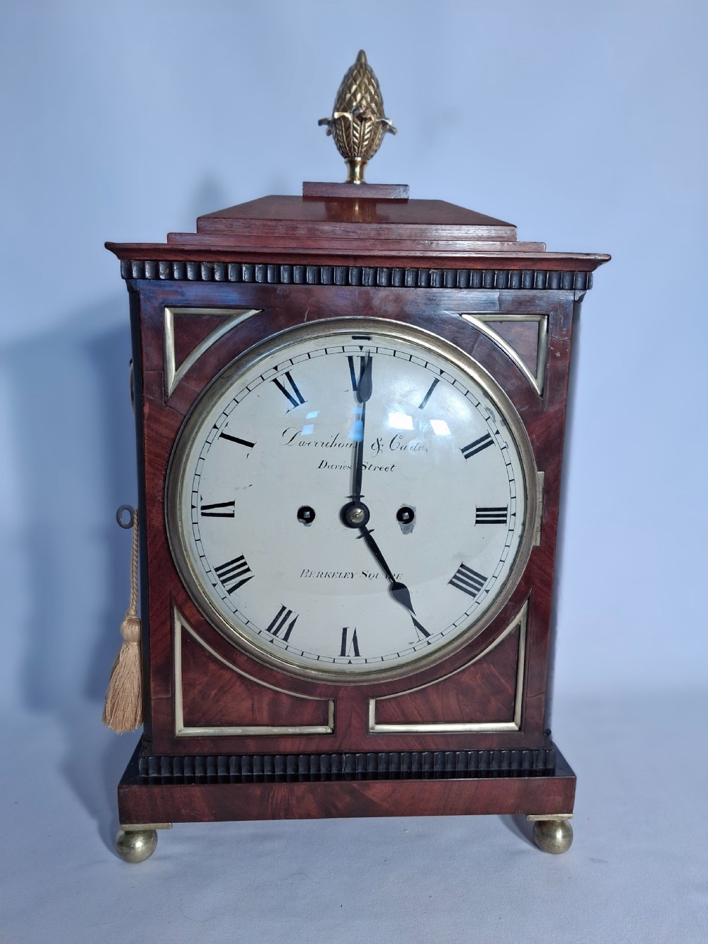 A George III mahogany bracket clock featuring a brass pineapple finial, brass corner spandrels, ball feet, and a white dial with Roman numerals.