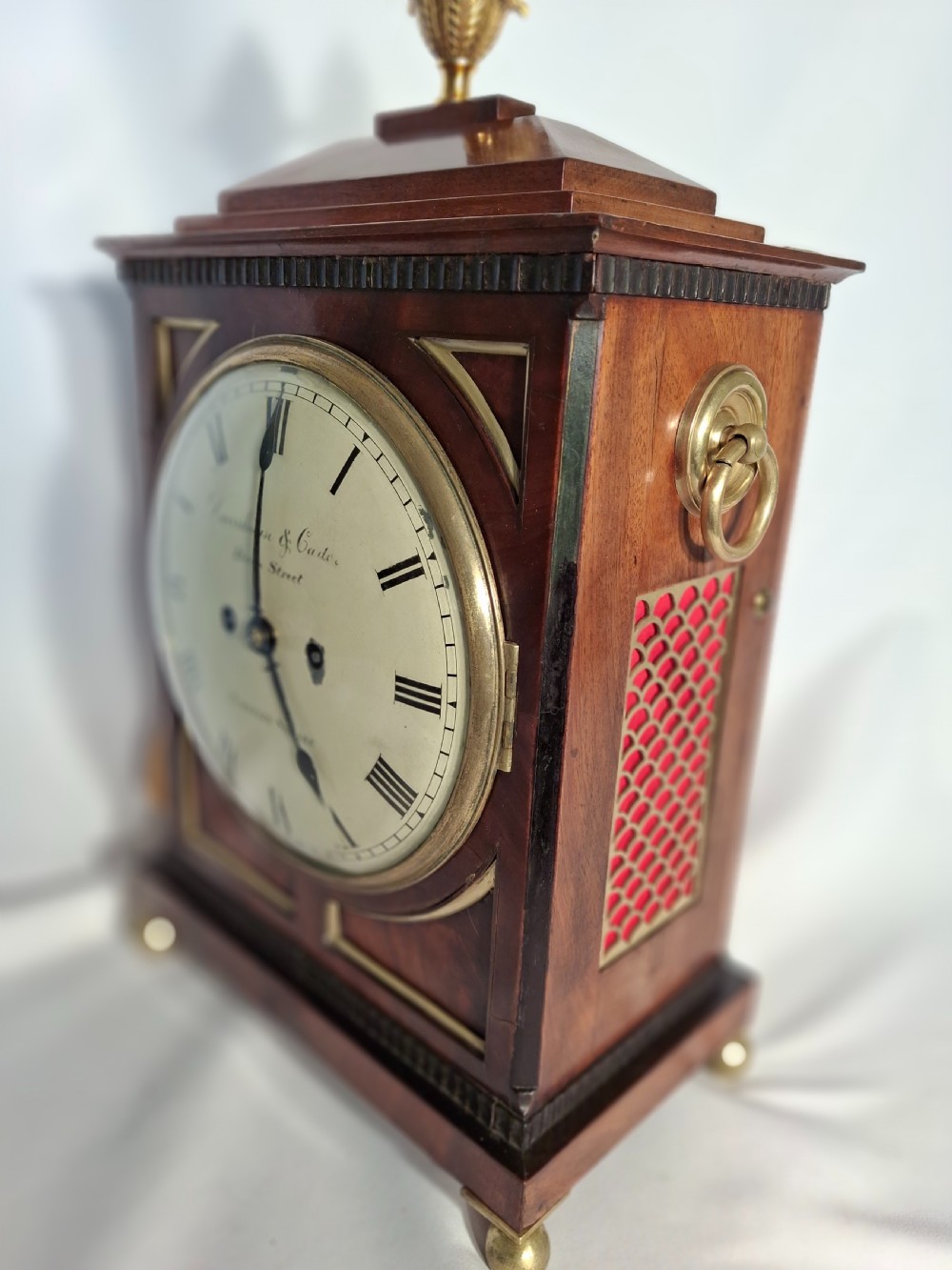 A George III mahogany bracket clock featuring a brass pineapple finial, brass corner spandrels, ball feet, and a white dial with Roman numerals. View III