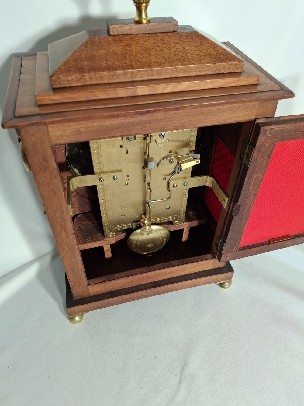 A George III mahogany bracket clock featuring a brass pineapple finial, brass corner spandrels, ball feet, and a white dial with Roman numerals. View VI