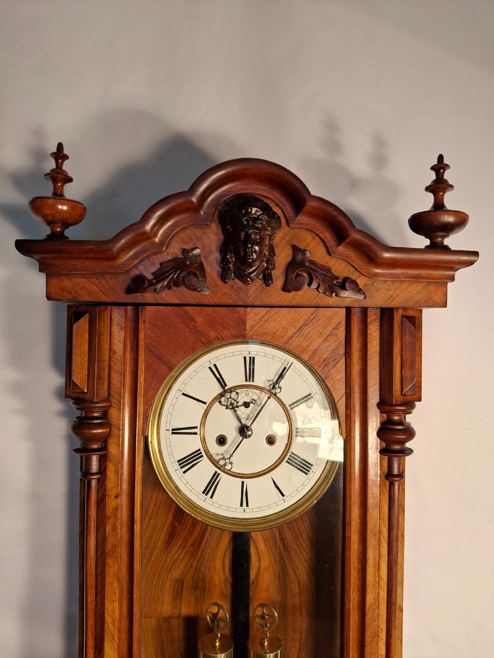 An antique walnut double-weight Vienna regulator wall clock featuring a white enamel dial with Roman numerals, visible brass weights, and a brass pendulum inside a glazed case with turned finials. View II