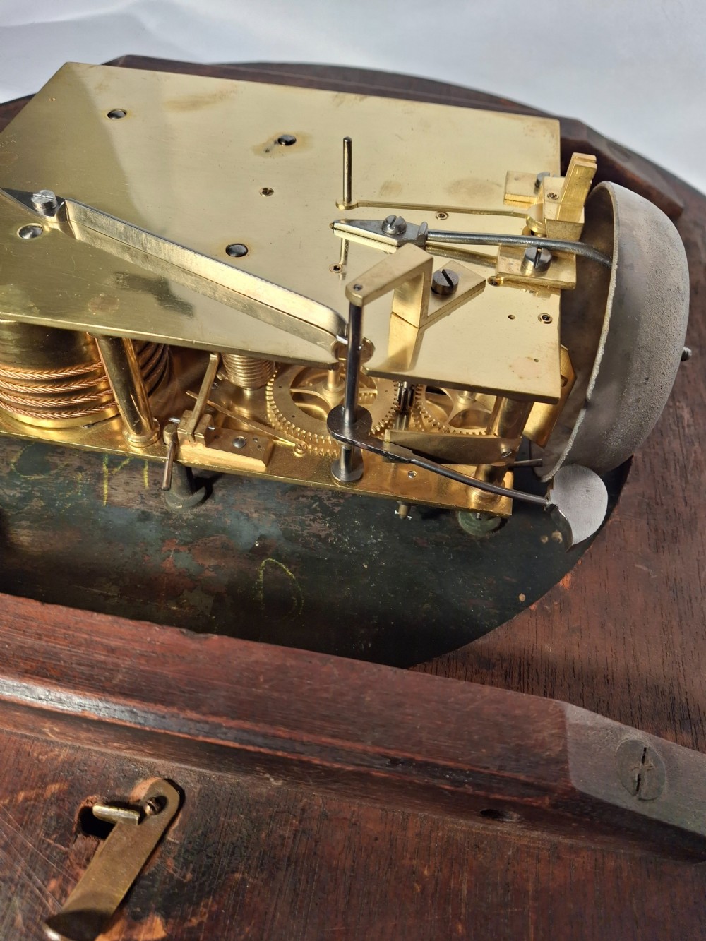 A Victorian mahogany drop-dial wall clock featuring brass floral inlay surrounding the dial and a glazed lower aperture showing a brass pendulum. View IV