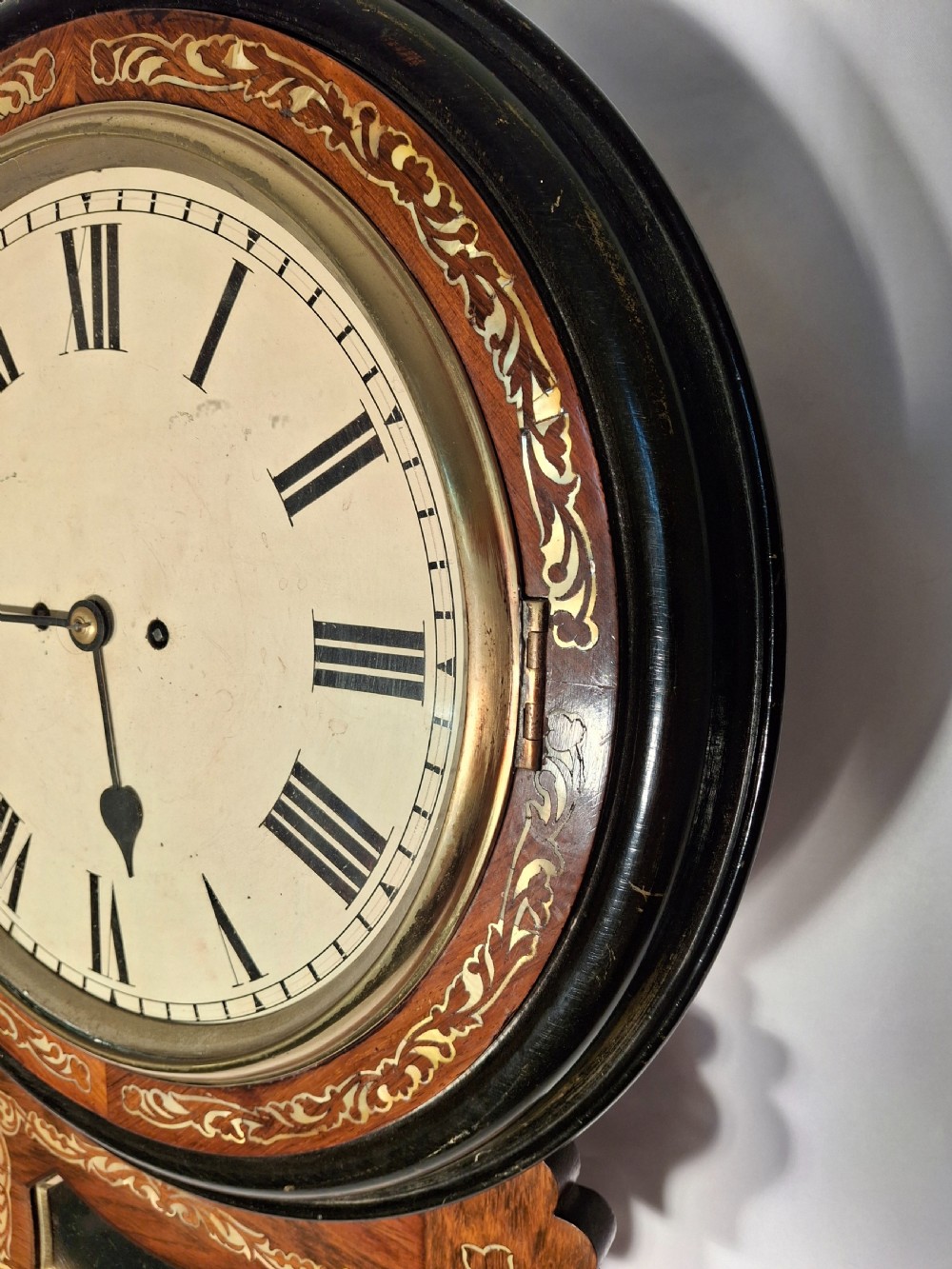 A Victorian mahogany drop-dial wall clock featuring brass floral inlay surrounding the dial and a glazed lower aperture showing a brass pendulum. View V