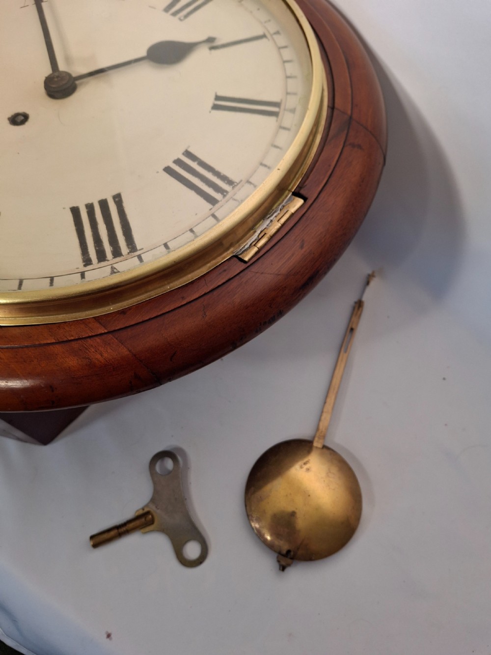 An antique circular mahogany wall clock featuring a brass bezel and a cream dial with black Roman numerals. View II