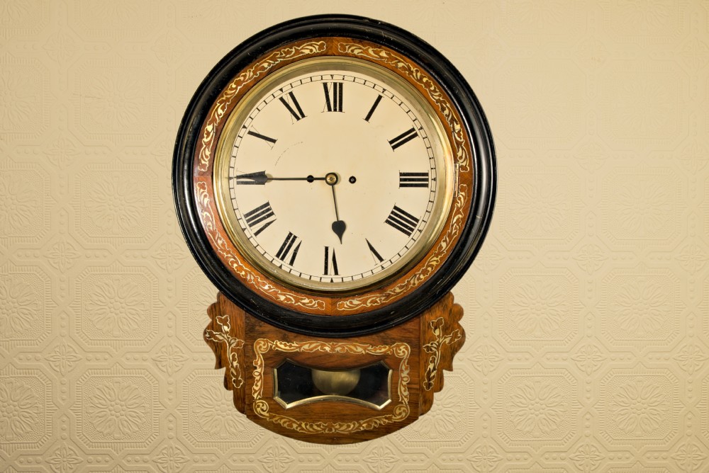 A Victorian mahogany drop-dial wall clock featuring brass floral inlay surrounding the dial and a glazed lower aperture showing a brass pendulum. View II