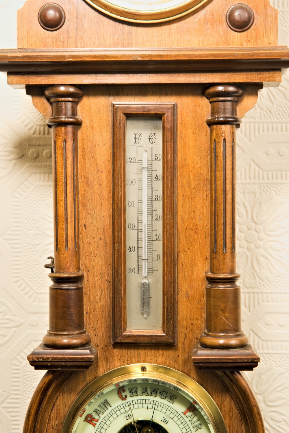 A wall-hung antique walnut clock, thermometer, and aneroid barometer companion set featuring carved pediment ornamentation and brass-rimmed dials. View V