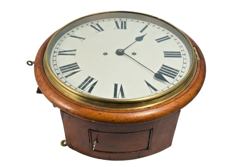 An antique round wall clock featuring a warm mahogany case, a polished brass bezel, and a white dial with black Roman numerals.