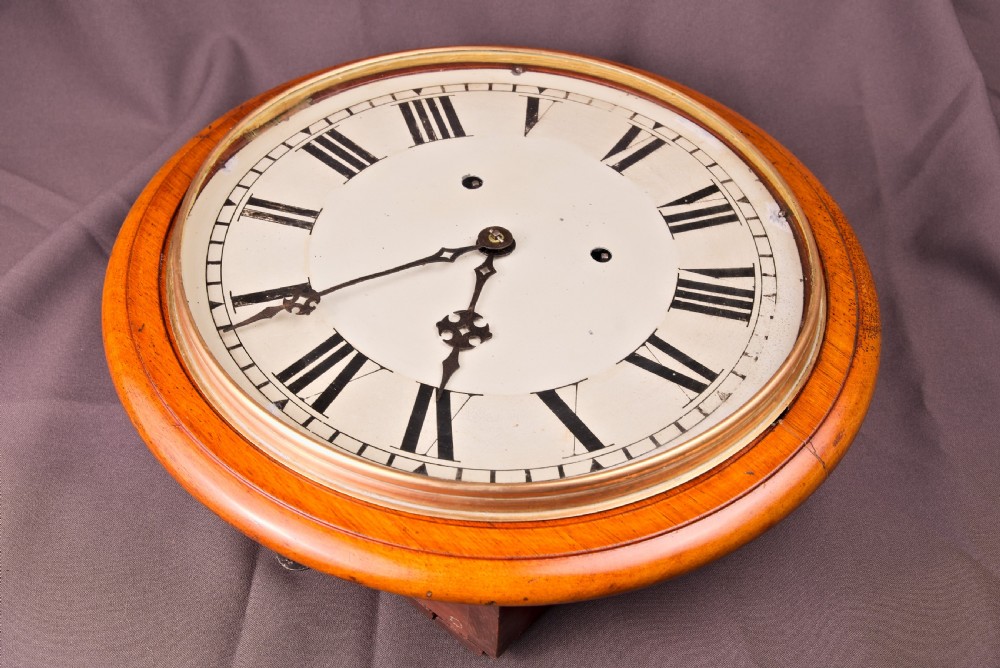 A circular antique wall clock featuring a golden oak turned surround, a white dial with black Roman numerals, brass bezel, and decorative black hands. View II