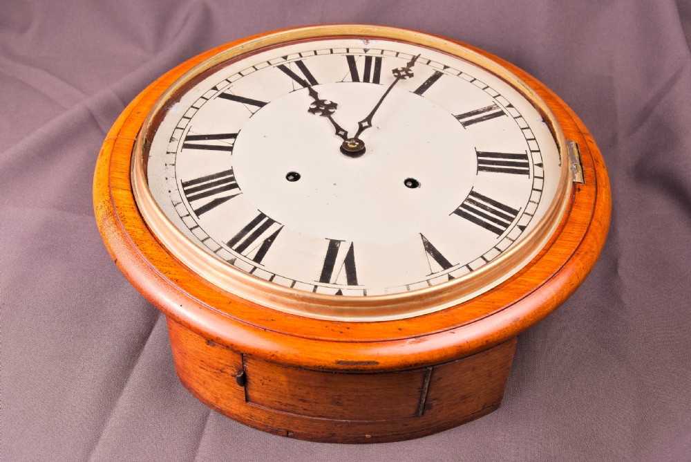 A circular antique wall clock featuring a golden oak turned surround, a white dial with black Roman numerals, brass bezel, and decorative black hands. View III