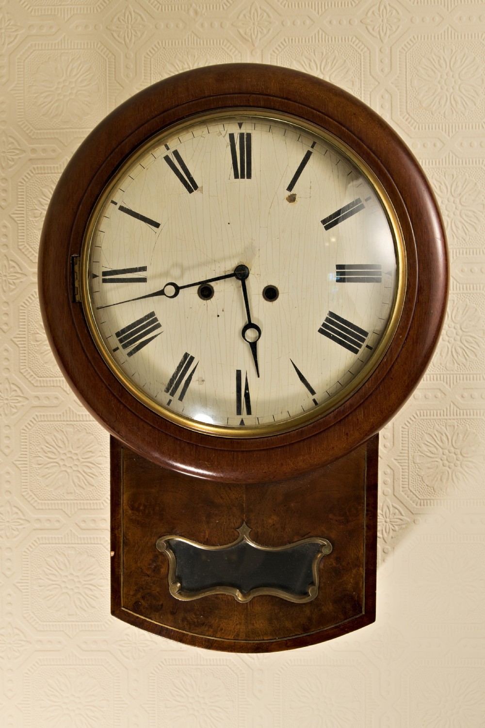 An antique Victorian drop-dial wall clock featuring a circular mahogany frame, cream dial with Roman numerals, and a lower wooden trunk with a brass aperture. View II