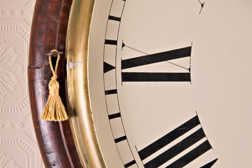A large circular antique wall clock featuring a dark mahogany surround, turned brass bezel, and a cream dial with black Roman numerals. View III