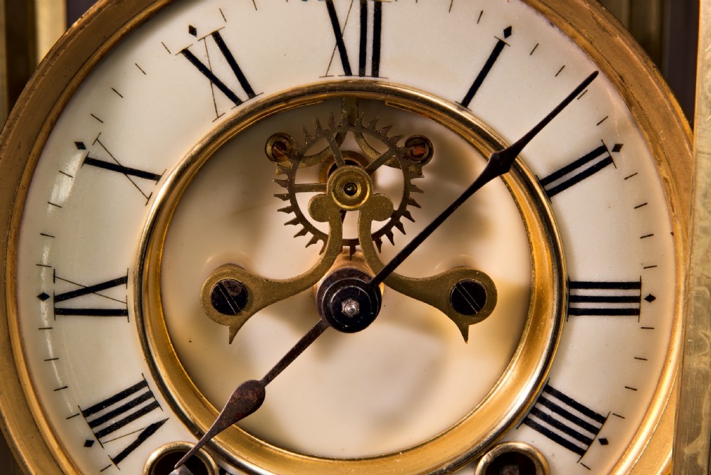 A 19th-century Rococo Revival gilt bronze four-glass mantel clock featuring scrollwork cresting, a white enamel dial, and a visible mercury pendulum. View IV