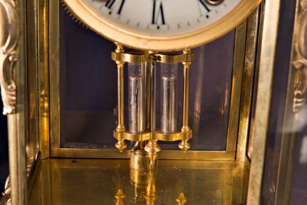 A 19th-century Rococo Revival gilt bronze four-glass mantel clock featuring scrollwork cresting, a white enamel dial, and a visible mercury pendulum. View VI