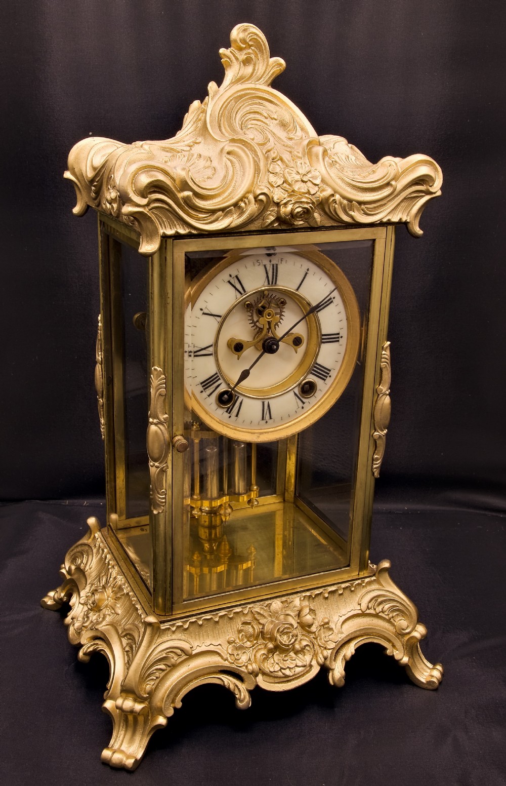 A 19th-century Rococo Revival gilt bronze four-glass mantel clock featuring scrollwork cresting, a white enamel dial, and a visible mercury pendulum. View X