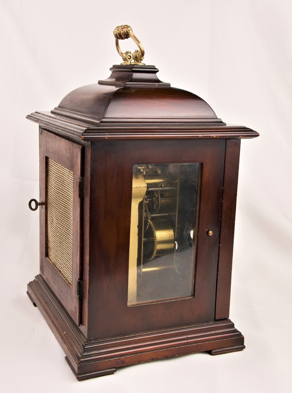 A dark mahogany wooden bracket mantel clock featuring a brass dial with Roman numerals, cast brass spandrels, glass side panels, and a brass carrying handle on top. View II
