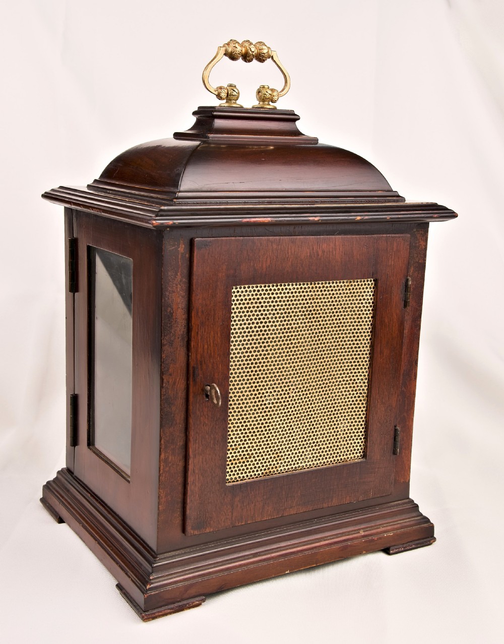 A dark mahogany wooden bracket mantel clock featuring a brass dial with Roman numerals, cast brass spandrels, glass side panels, and a brass carrying handle on top. View III