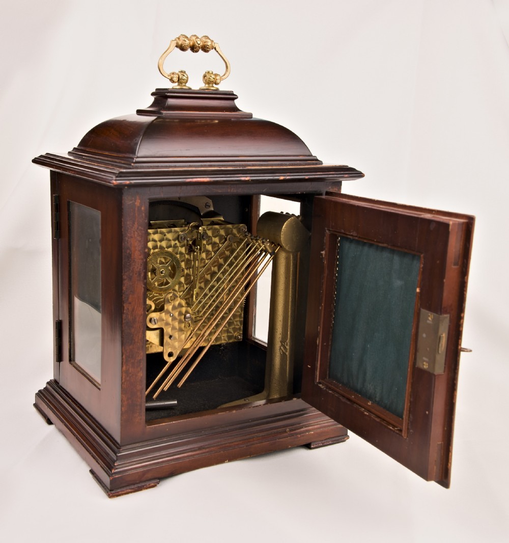 A dark mahogany wooden bracket mantel clock featuring a brass dial with Roman numerals, cast brass spandrels, glass side panels, and a brass carrying handle on top. View IV