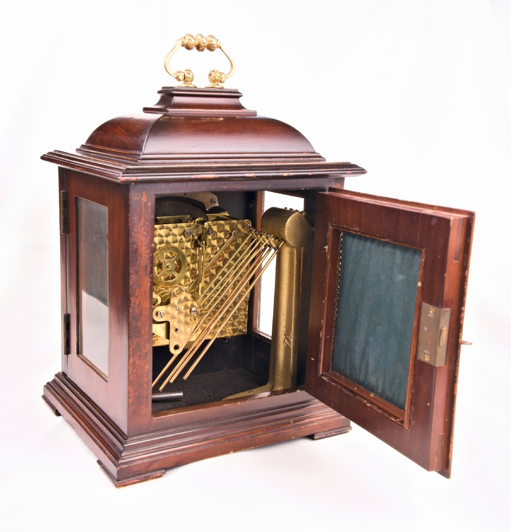 A dark mahogany wooden bracket mantel clock featuring a brass dial with Roman numerals, cast brass spandrels, glass side panels, and a brass carrying handle on top. View V