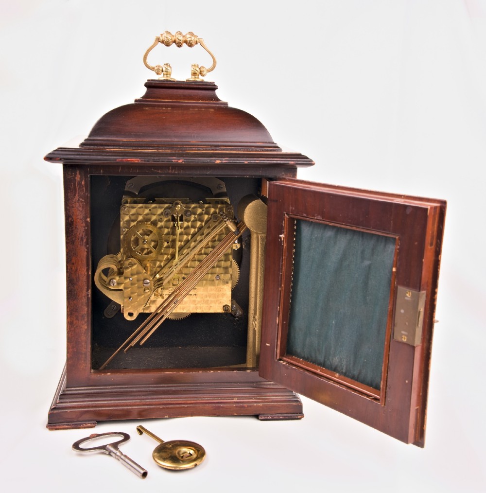 A dark mahogany wooden bracket mantel clock featuring a brass dial with Roman numerals, cast brass spandrels, glass side panels, and a brass carrying handle on top. View VI