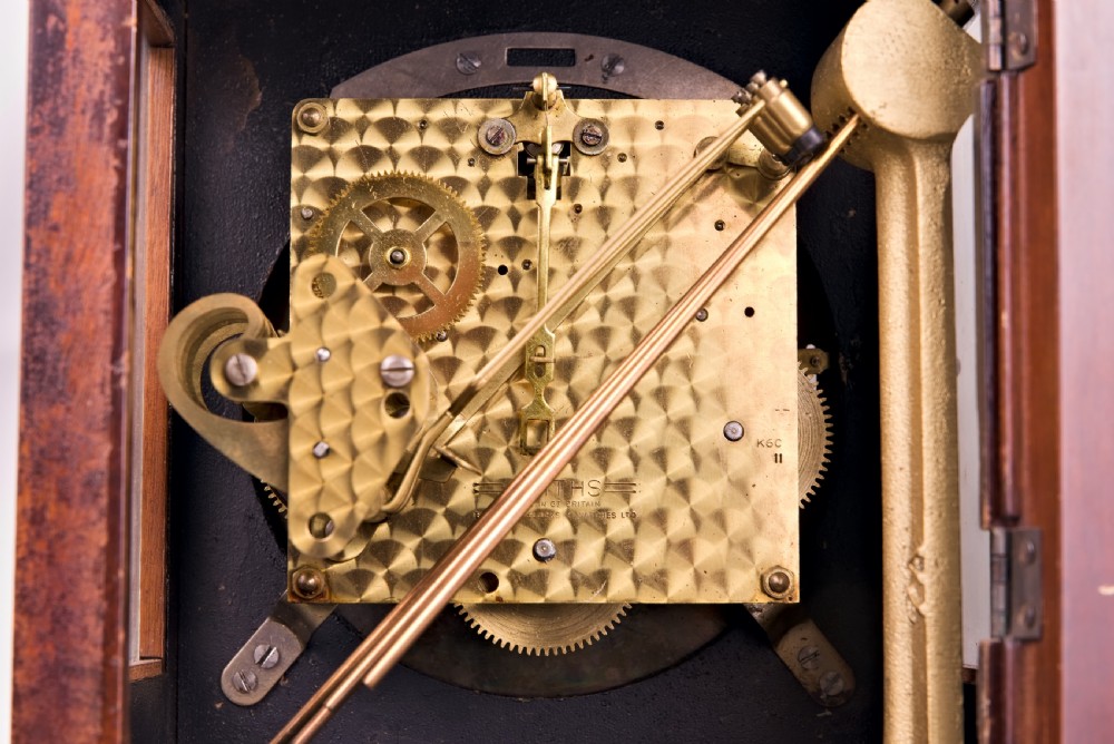 A dark mahogany wooden bracket mantel clock featuring a brass dial with Roman numerals, cast brass spandrels, glass side panels, and a brass carrying handle on top. View VII