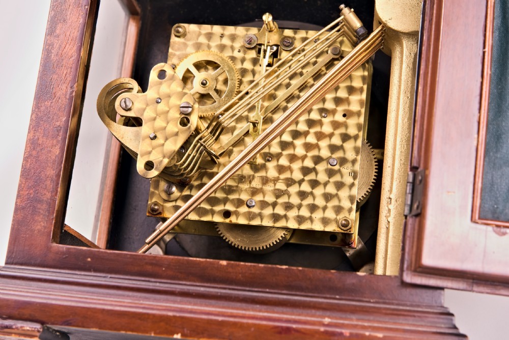 A dark mahogany wooden bracket mantel clock featuring a brass dial with Roman numerals, cast brass spandrels, glass side panels, and a brass carrying handle on top. View VIII
