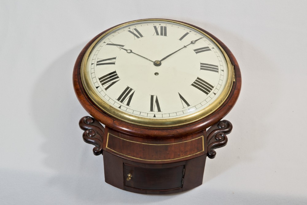 A Victorian mahogany fusee wall clock featuring a cream painted dial with Roman numerals, a brass bezel, and carved side scroll ears.