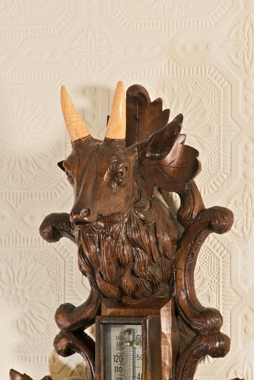 A late 19th-century Black Forest carved wooden wall barometer featuring a chamois head at the top, flanked by carved game animals and foliage around a central dial and upper thermometer tube. View II