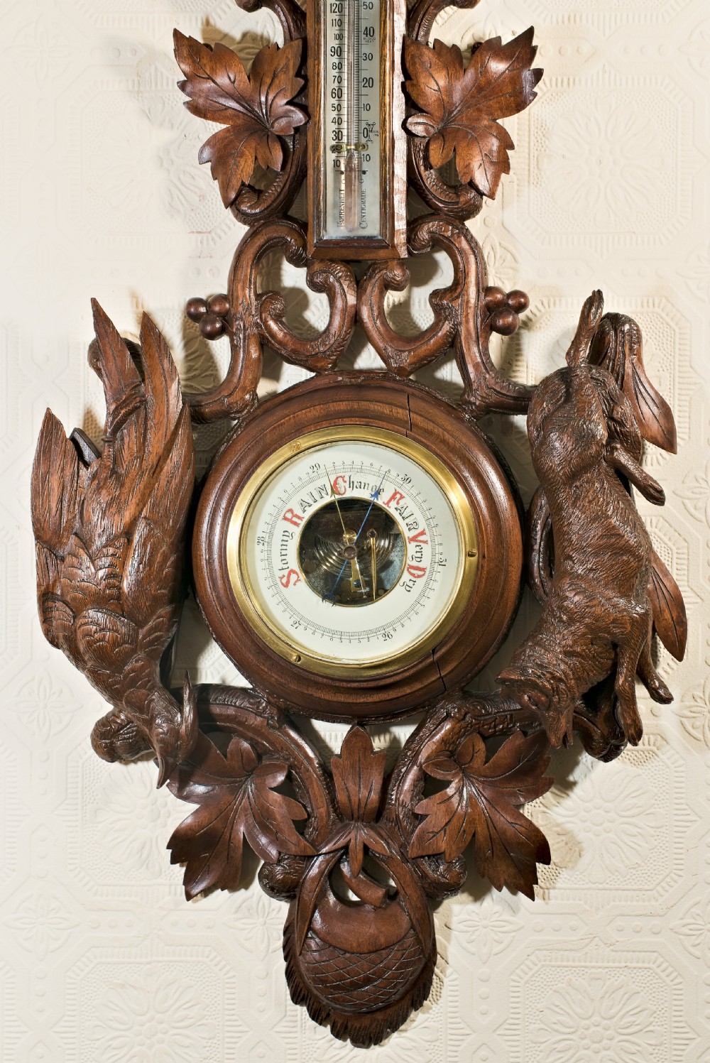 A late 19th-century Black Forest carved wooden wall barometer featuring a chamois head at the top, flanked by carved game animals and foliage around a central dial and upper thermometer tube. View VII