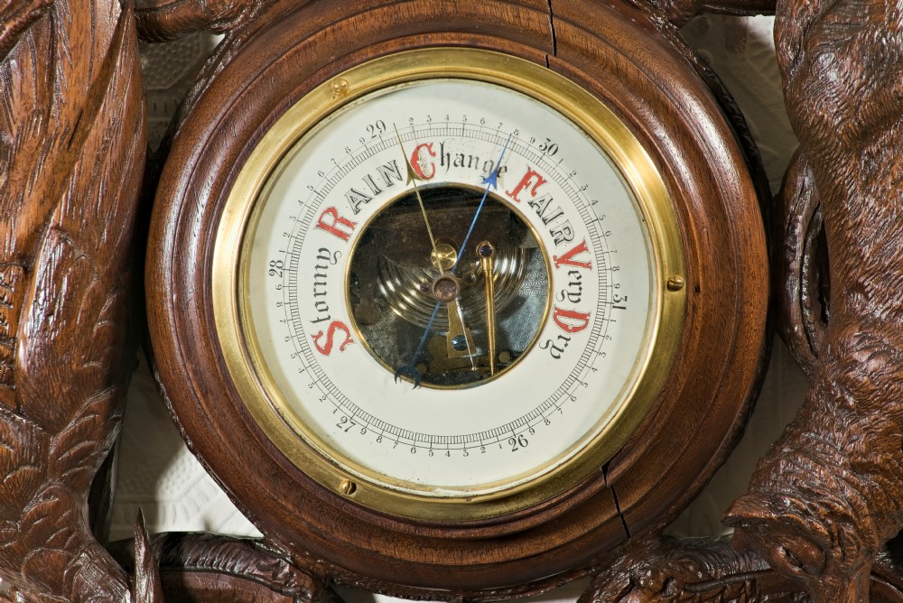 A late 19th-century Black Forest carved wooden wall barometer featuring a chamois head at the top, flanked by carved game animals and foliage around a central dial and upper thermometer tube. View VIII