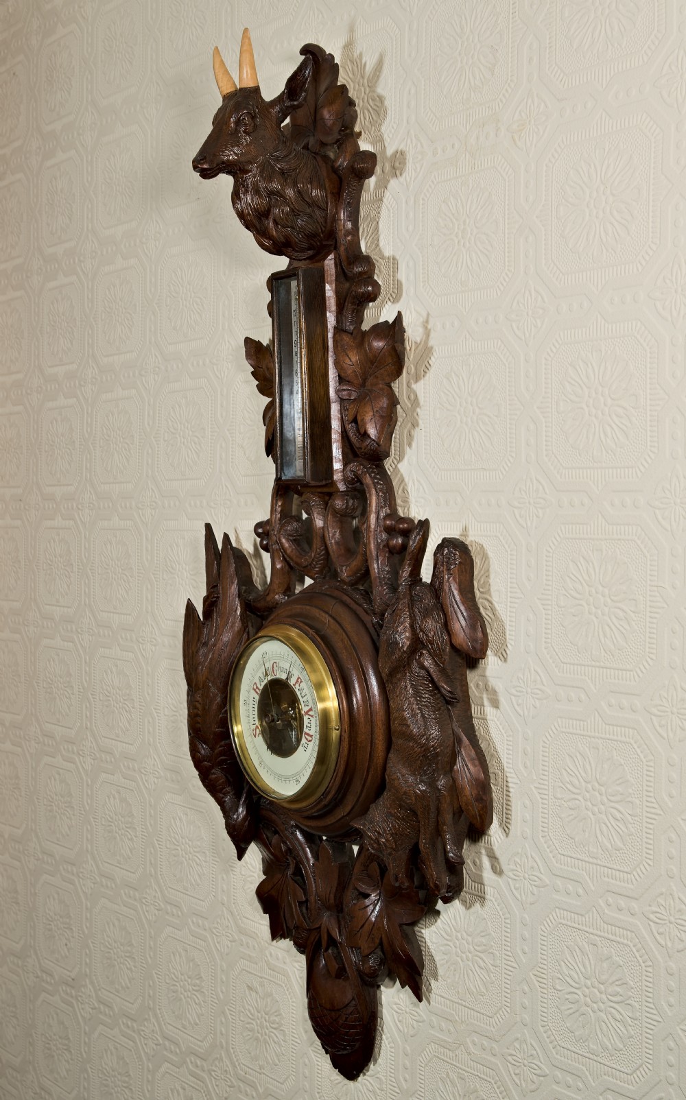 A late 19th-century Black Forest carved wooden wall barometer featuring a chamois head at the top, flanked by carved game animals and foliage around a central dial and upper thermometer tube. View XI