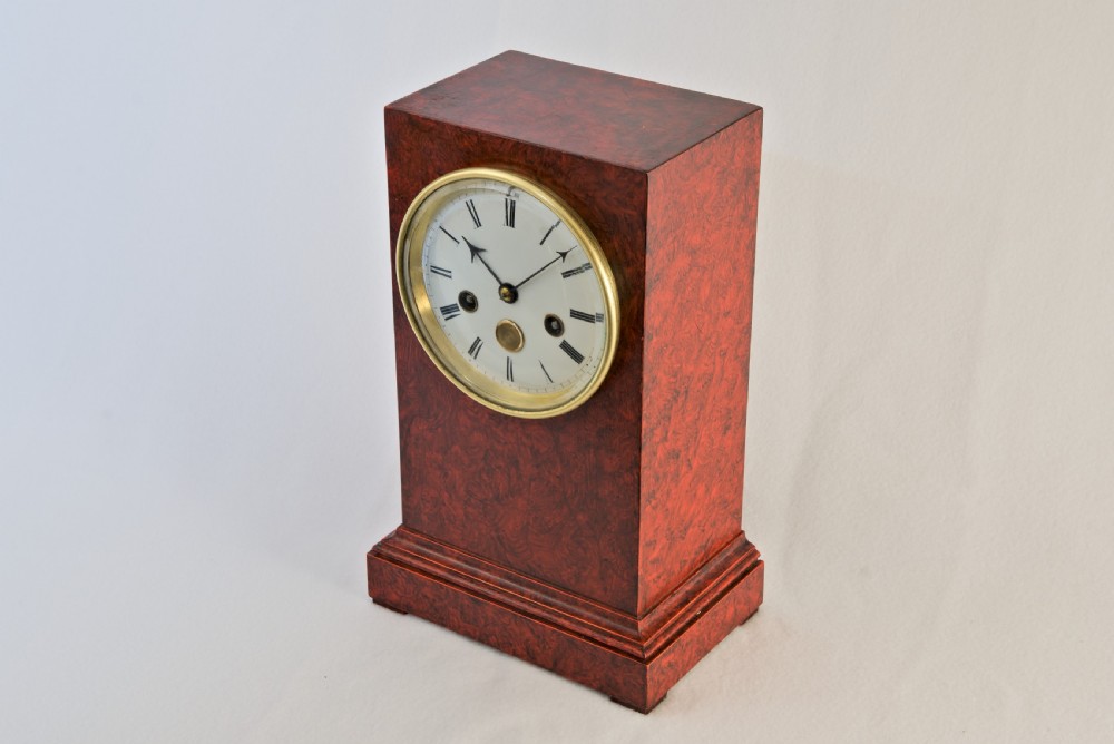 An upright rectangular clock featuring a mottled red faux tortoiseshell case, a stepped base, and a circular white enamel dial framed by a brass bezel. View IV