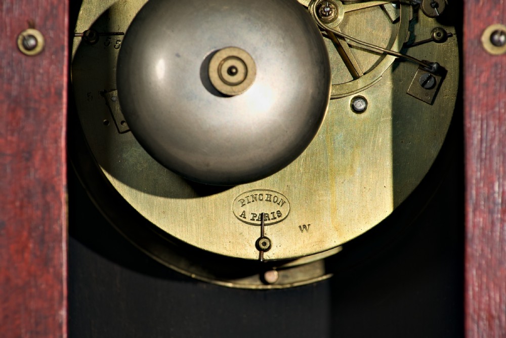 An upright rectangular clock featuring a mottled red faux tortoiseshell case, a stepped base, and a circular white enamel dial framed by a brass bezel. View VIII