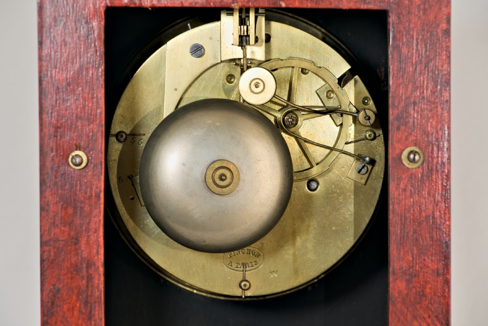 An upright rectangular clock featuring a mottled red faux tortoiseshell case, a stepped base, and a circular white enamel dial framed by a brass bezel. View IX