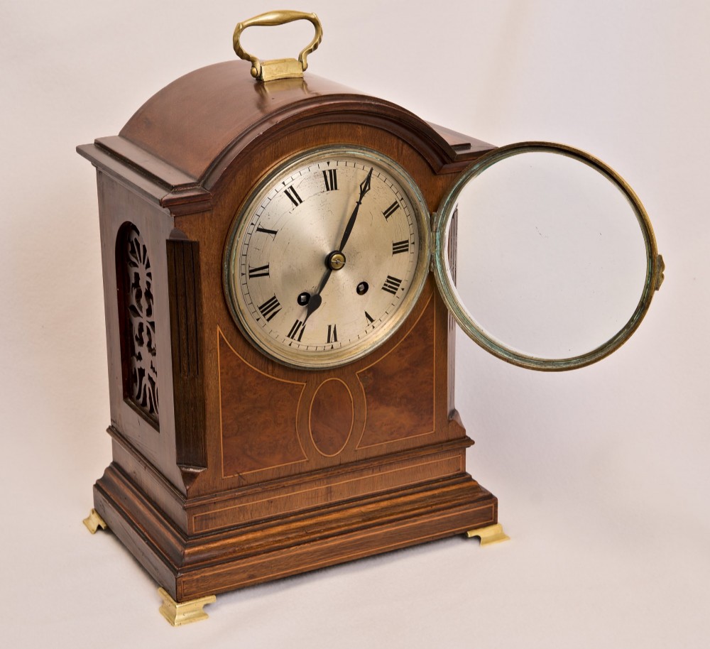 An Edwardian inlaid mahogany arch-top mantel clock with a brass-bezel dial, Roman numerals, side sound frets, and brass corner feet. View II