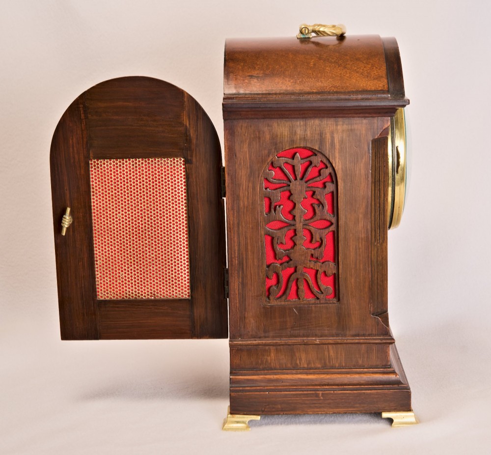 An Edwardian inlaid mahogany arch-top mantel clock with a brass-bezel dial, Roman numerals, side sound frets, and brass corner feet. View V