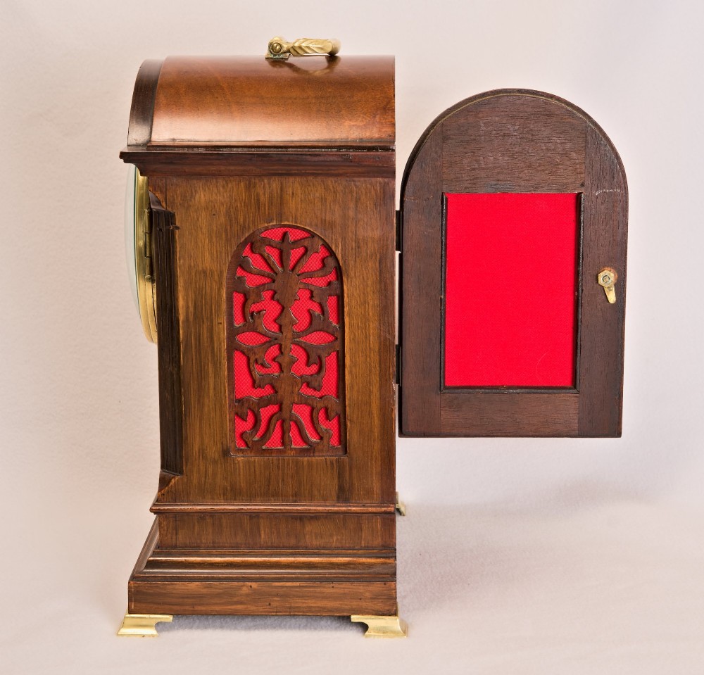An Edwardian inlaid mahogany arch-top mantel clock with a brass-bezel dial, Roman numerals, side sound frets, and brass corner feet. View VI