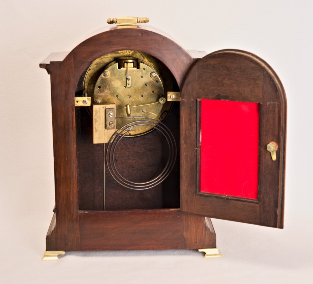 An Edwardian inlaid mahogany arch-top mantel clock with a brass-bezel dial, Roman numerals, side sound frets, and brass corner feet. View VII