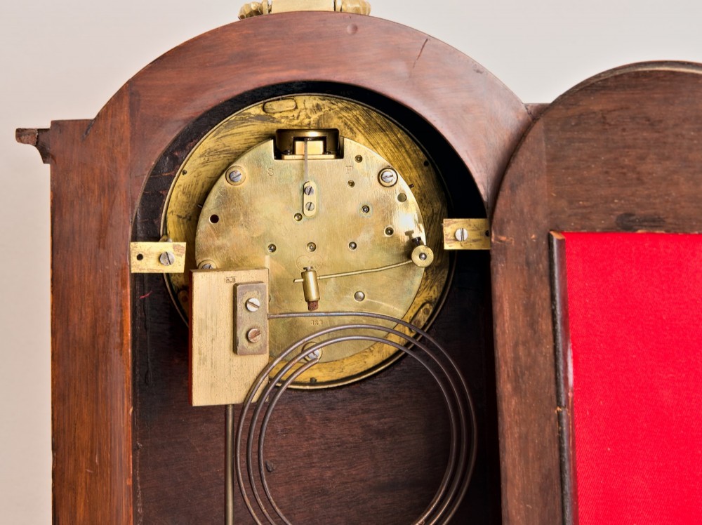 An Edwardian inlaid mahogany arch-top mantel clock with a brass-bezel dial, Roman numerals, side sound frets, and brass corner feet. View VIII