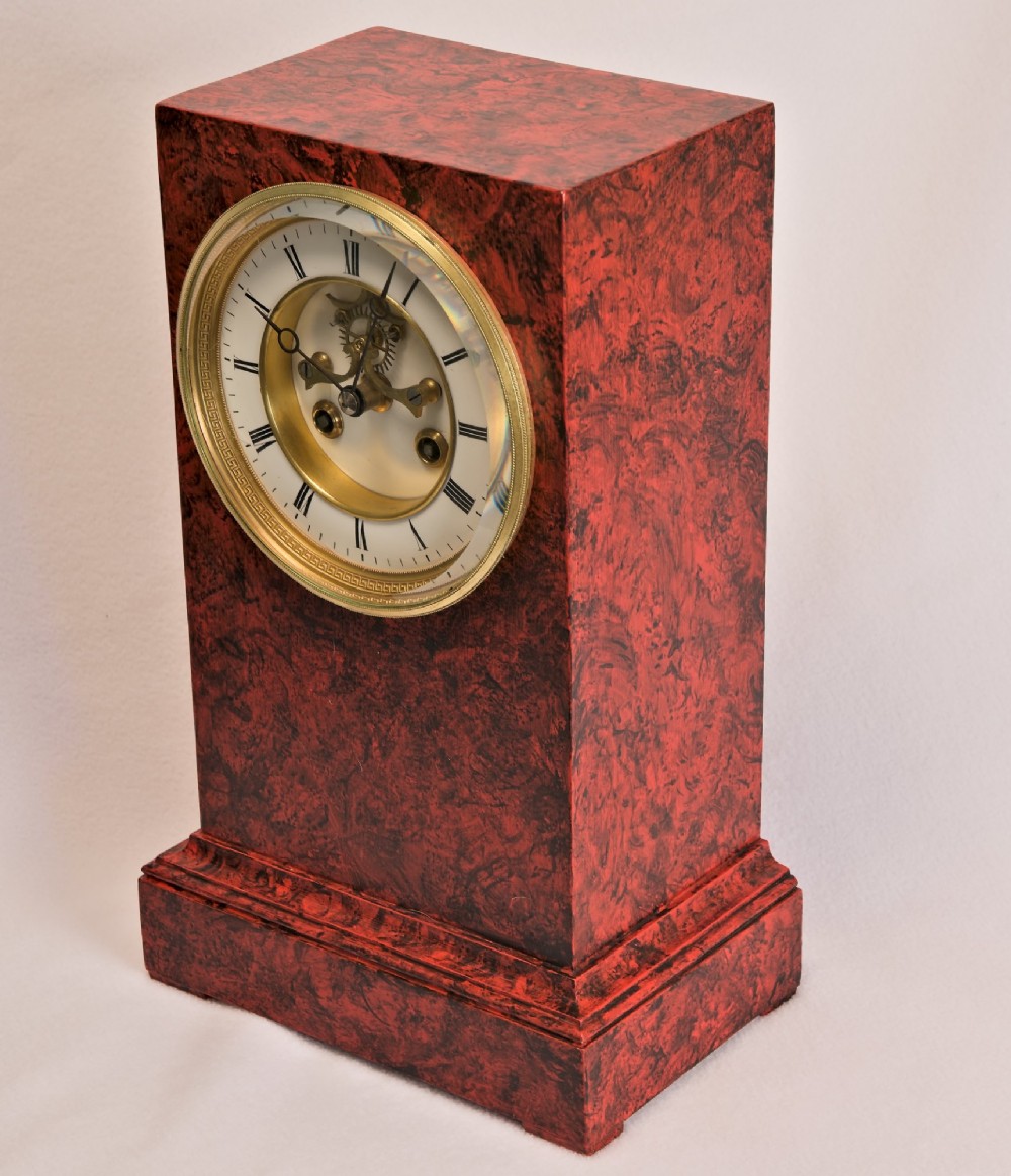 A rectangular mantel clock featuring a red and black faux tortoiseshell finish, a circular brass-framed dial with Roman numerals, and a visible central movement mechanism. View II