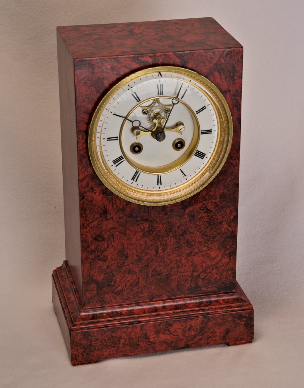 A rectangular mantel clock featuring a red and black faux tortoiseshell finish, a circular brass-framed dial with Roman numerals, and a visible central movement mechanism. View III