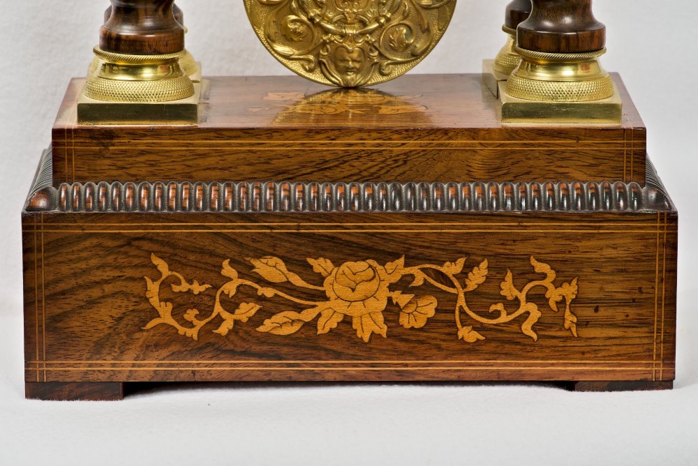 A 19th-century rosewood portico clock featuring floral marquetry inlays, twin barley-twist columns with gilt capitals, and a white enamel dial with an ornate gilt bezel. View V