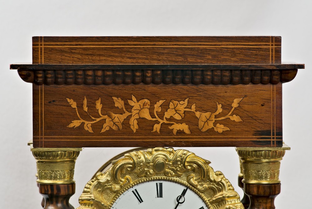 A 19th-century rosewood portico clock featuring floral marquetry inlays, twin barley-twist columns with gilt capitals, and a white enamel dial with an ornate gilt bezel. View VI