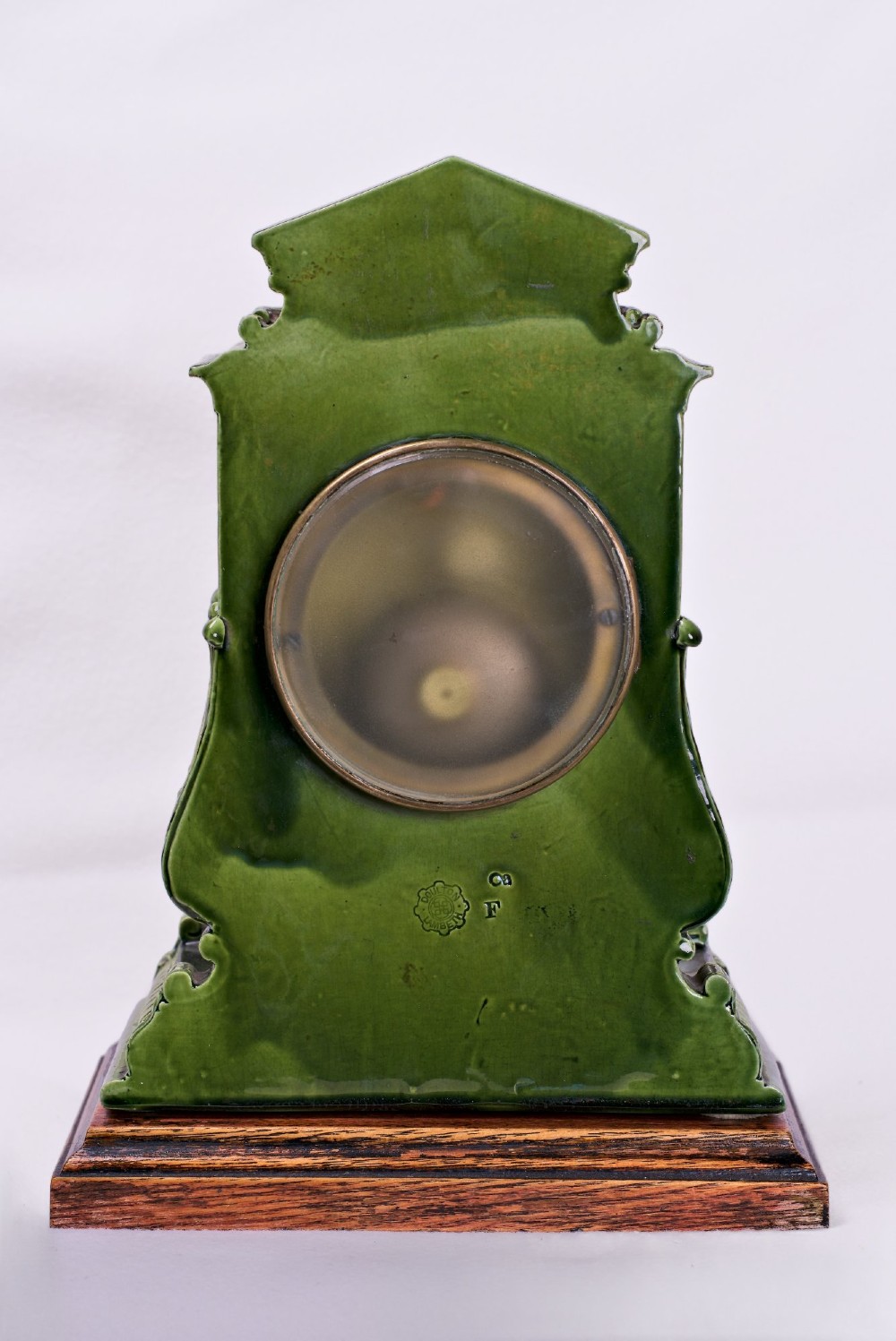 An olive green glazed ceramic mantel clock featuring relief acanthus foliage details, a white dial with blue Arabic numerals, mounted on a dark wooden base. View VIII