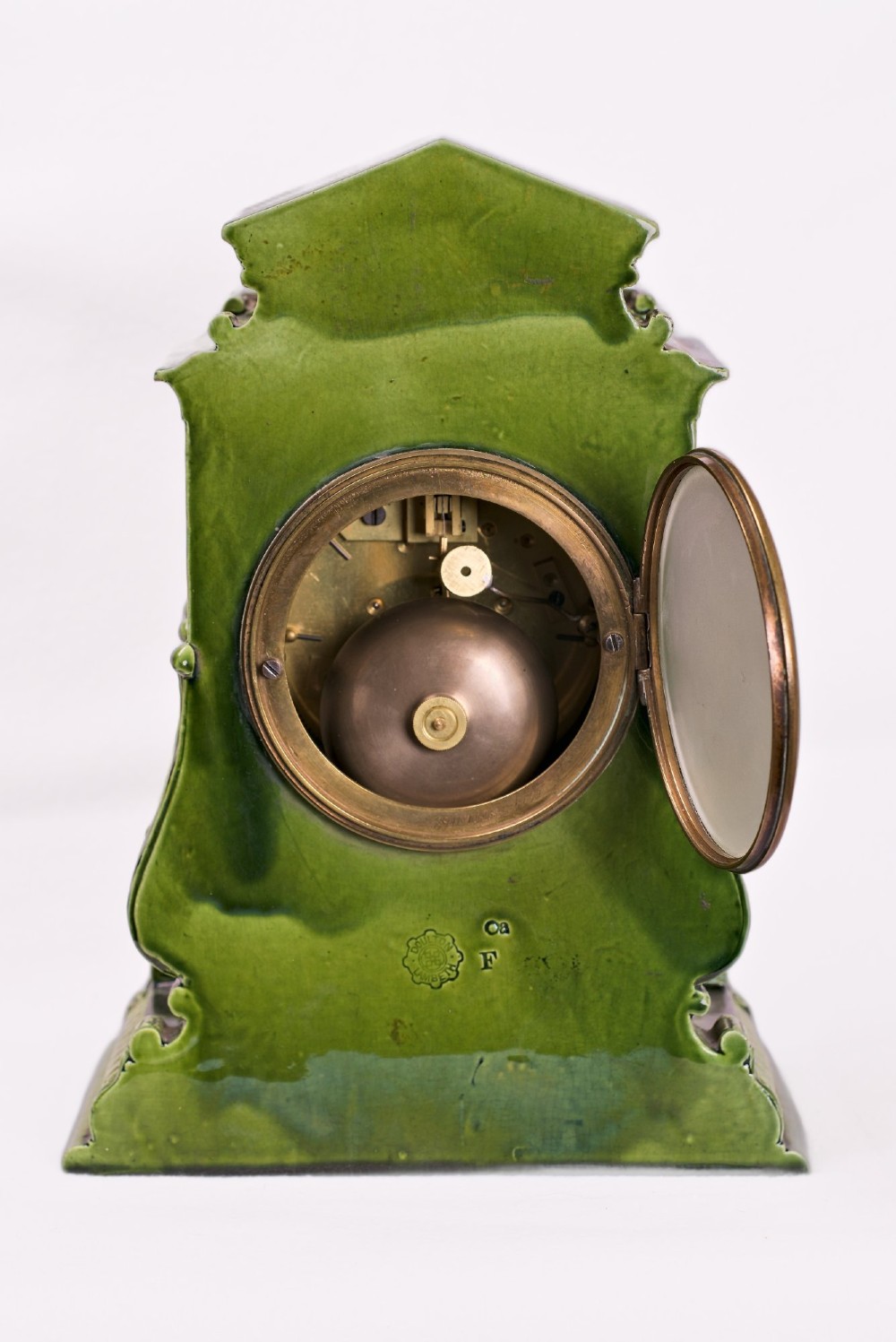 An olive green glazed ceramic mantel clock featuring relief acanthus foliage details, a white dial with blue Arabic numerals, mounted on a dark wooden base. View IX