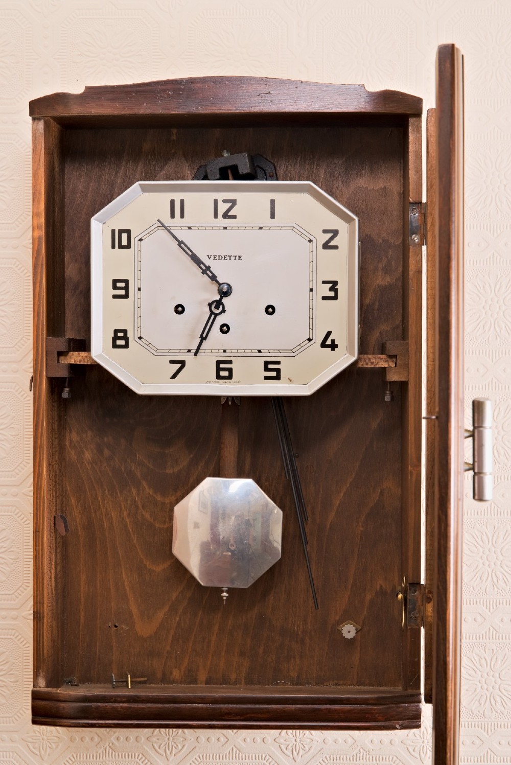 An Art Deco rectangular wooden wall clock featuring a light octagonal dial with Arabic numerals above a geometric leaded glass window. View II