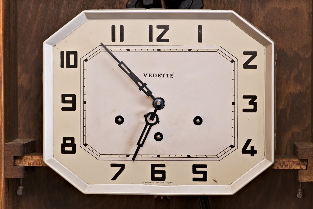 An Art Deco rectangular wooden wall clock featuring a light octagonal dial with Arabic numerals above a geometric leaded glass window. View III