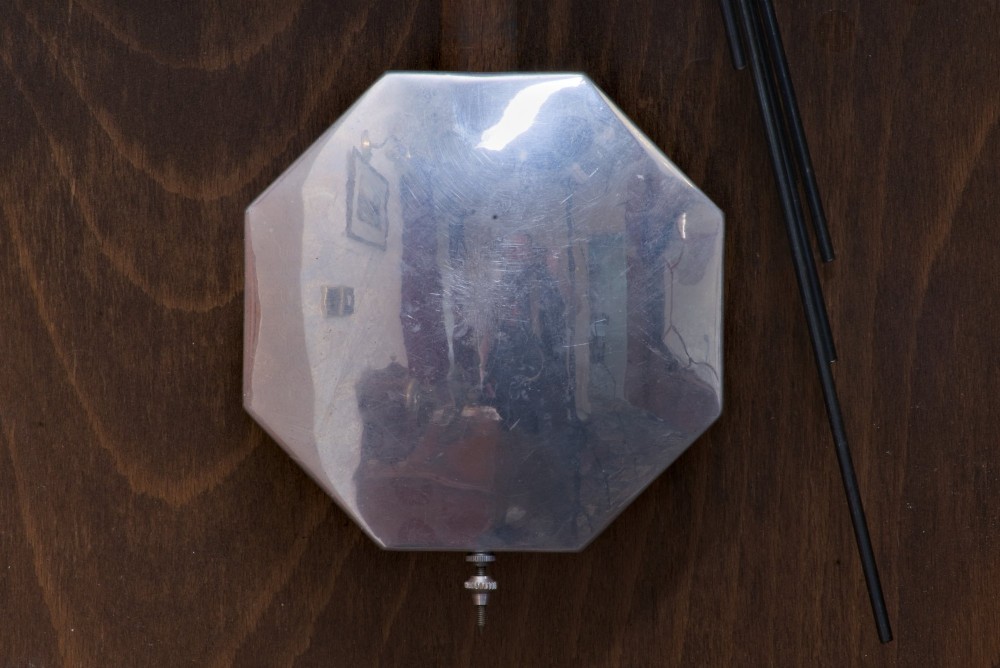 An Art Deco rectangular wooden wall clock featuring a light octagonal dial with Arabic numerals above a geometric leaded glass window. View IV